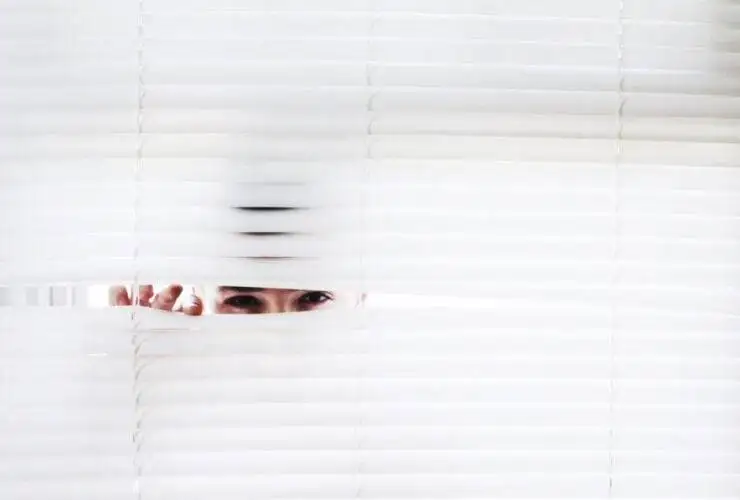 man spying through white blinds